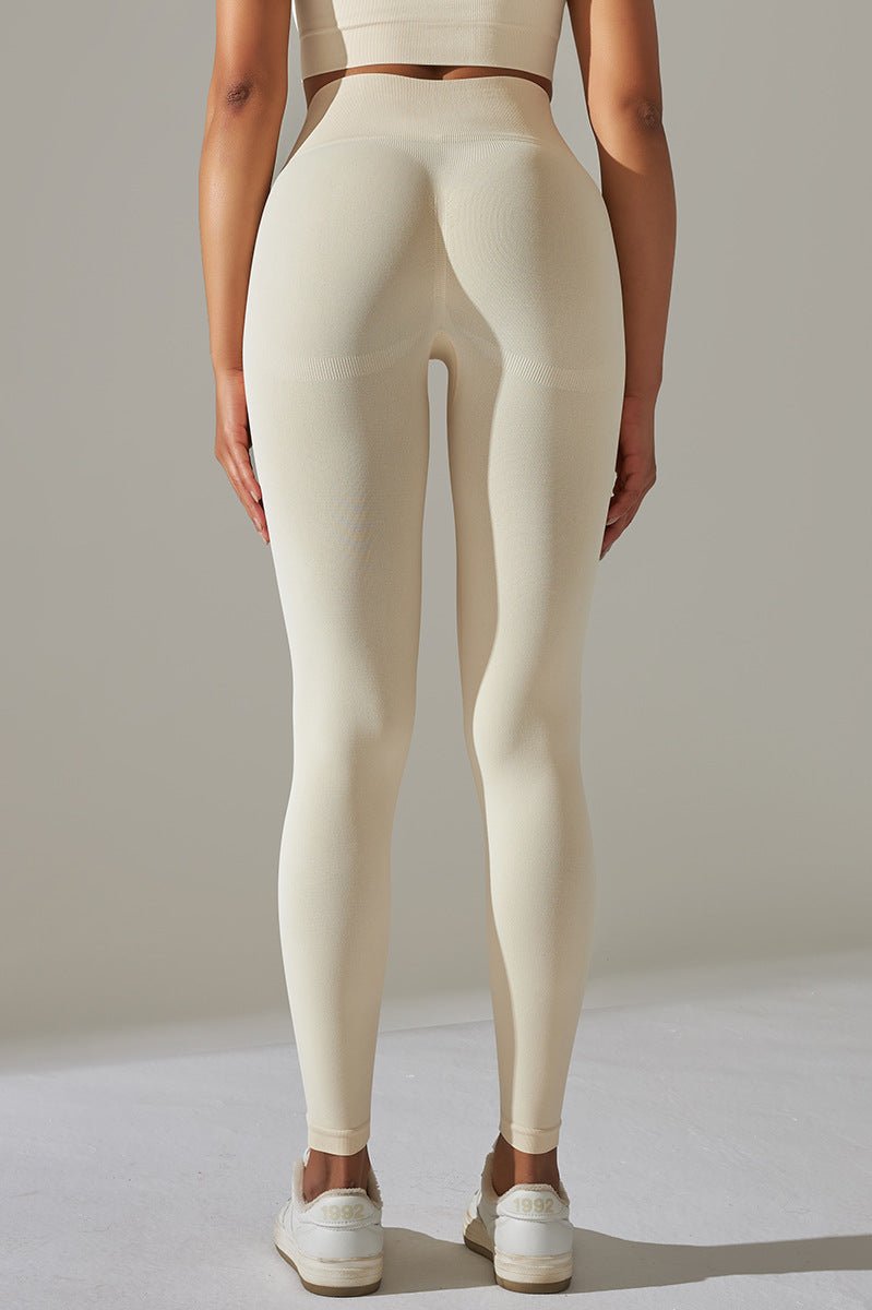 Kvinde i lyse leggings og crop top, poserer i fuld figur med én hånd på hoften.