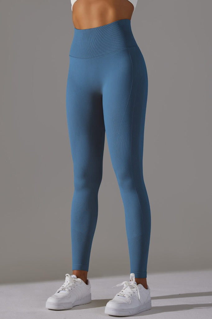 Kvinde iført blå scrunch tights med høj talje, stående i neutral positur. Billedet viser front og side af tights med sømløs pasform og teksturdetaljer.