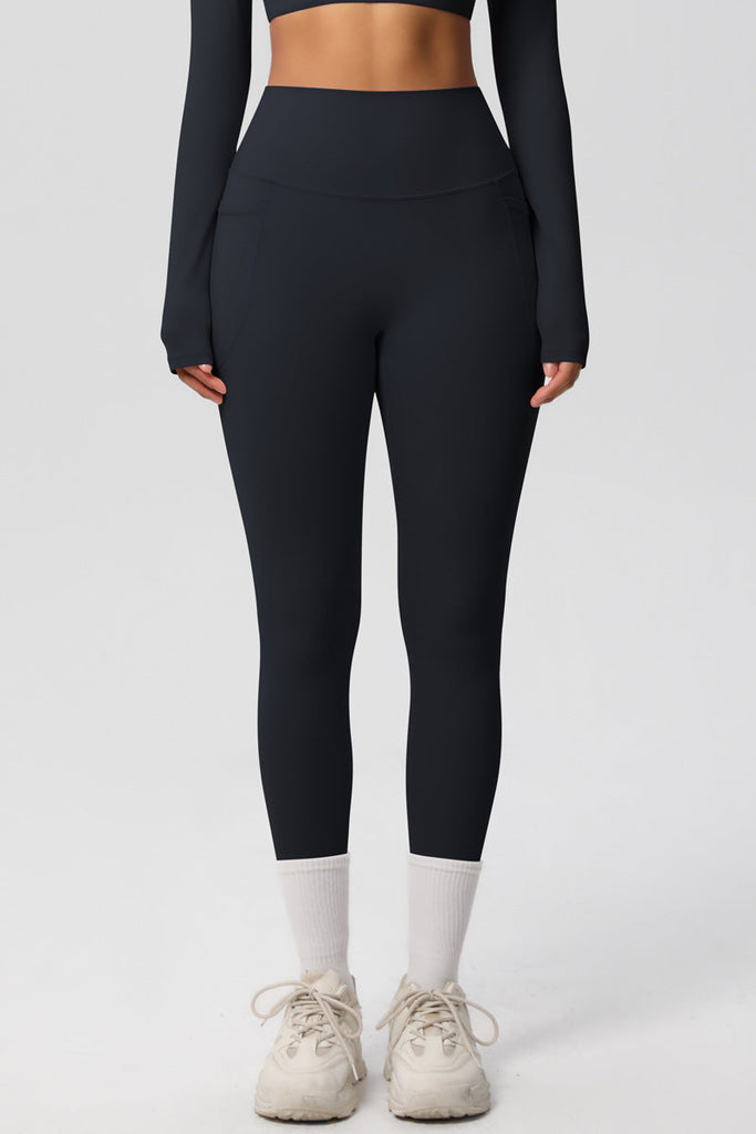 Model står i sorte leggings med høj talje – neutral baggrund og naturlig positur.