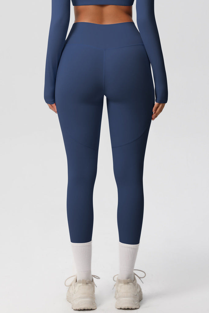 Model stående i blå leggings – set forfra i fuld figur med langærmet top og sneakers.

