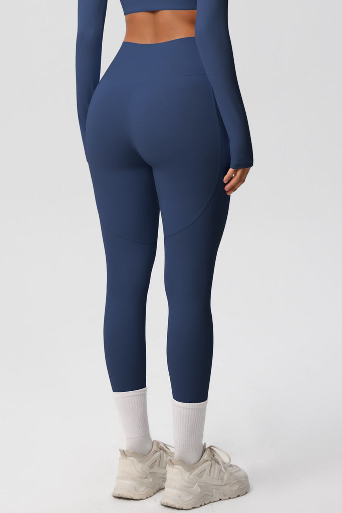 Model i blå leggings med høj talje og sidelommer – poserer afslappet med neutral baggrund.

