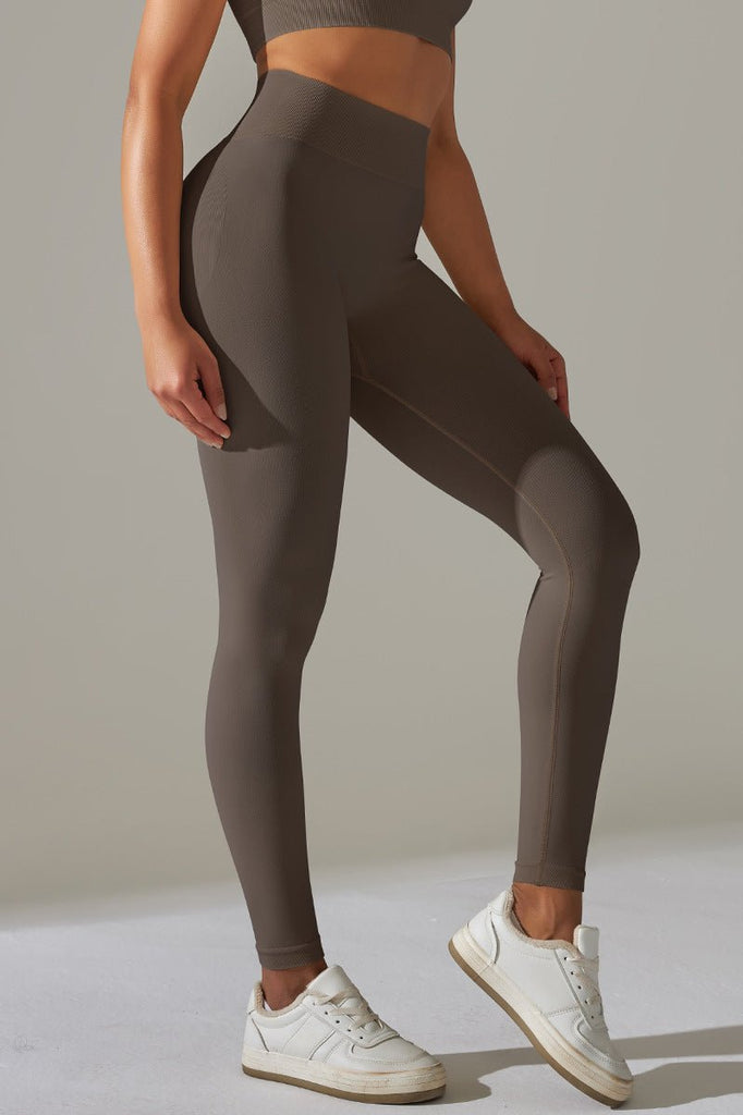 Kvinde i mørke scrunch leggings og top, står i helfigur med let bøjning i hoften og hænderne ved siden.

